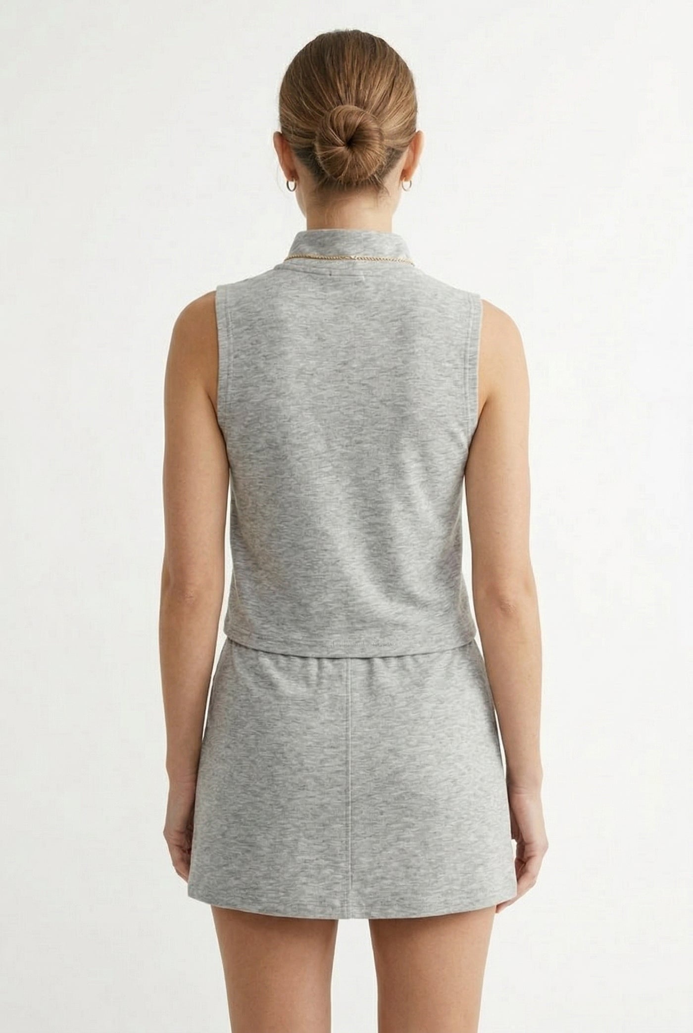 A woman wearing a Heather Light Gray sleeveless athletic dress with a zippered collar and matching skirt.