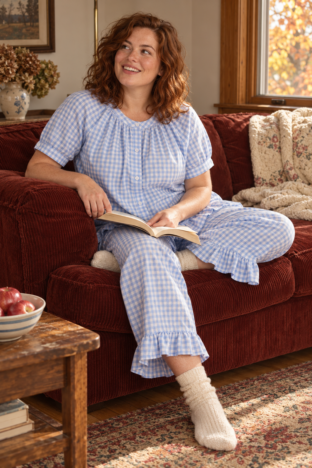 Woman wearing the powder blue Colette Gingham Set while reading on a red sofa.