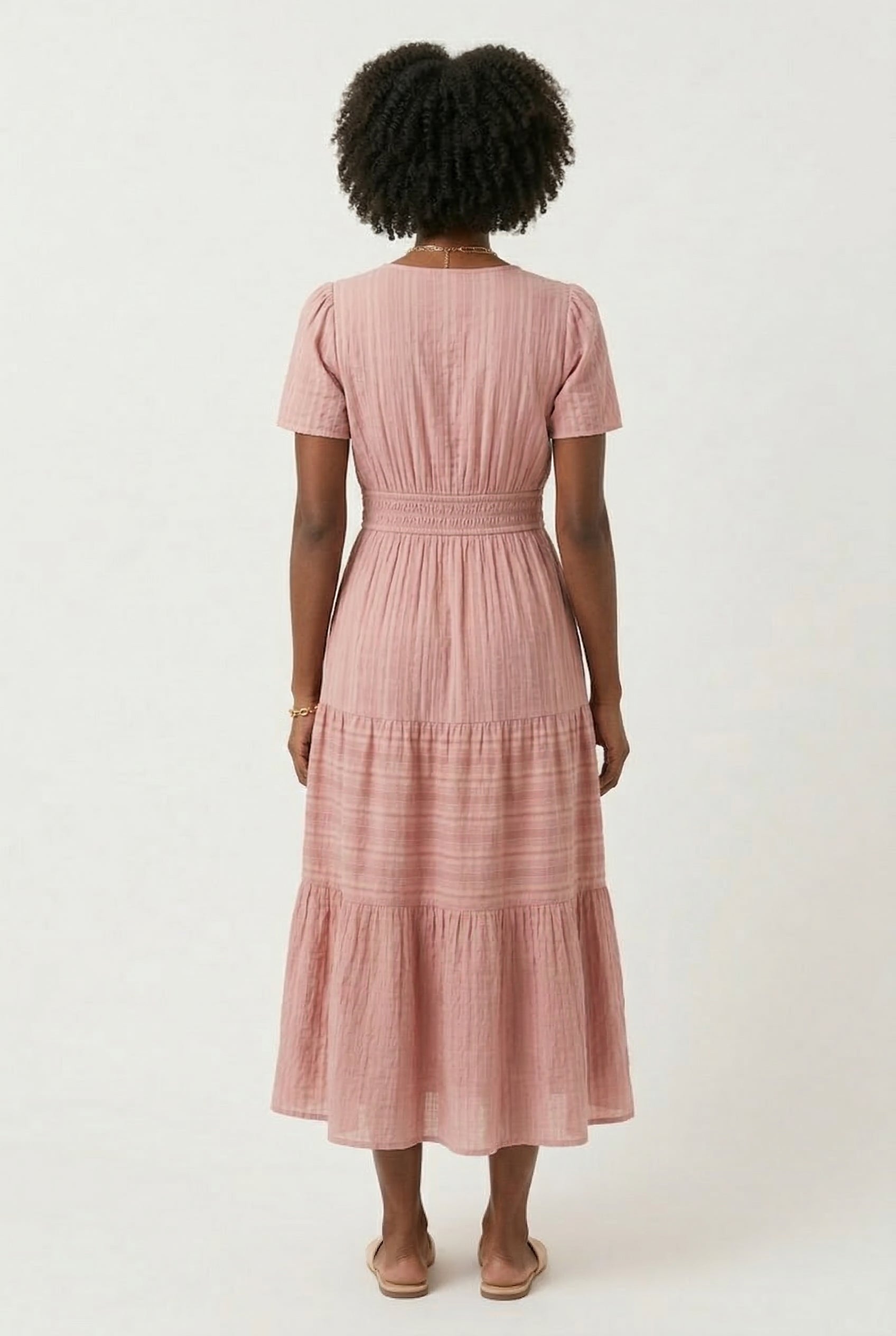 A woman wearing an Antique Pink short-sleeve midi dress with a button-up front and tiered hem.