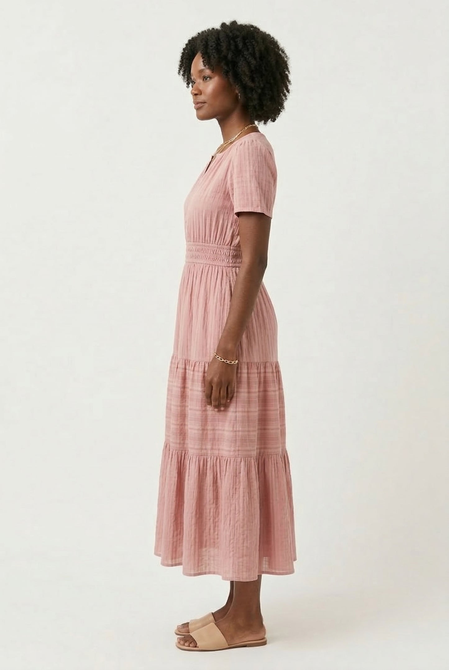 A woman wearing an Antique Pink short-sleeve midi dress with a button-up front and tiered hem.