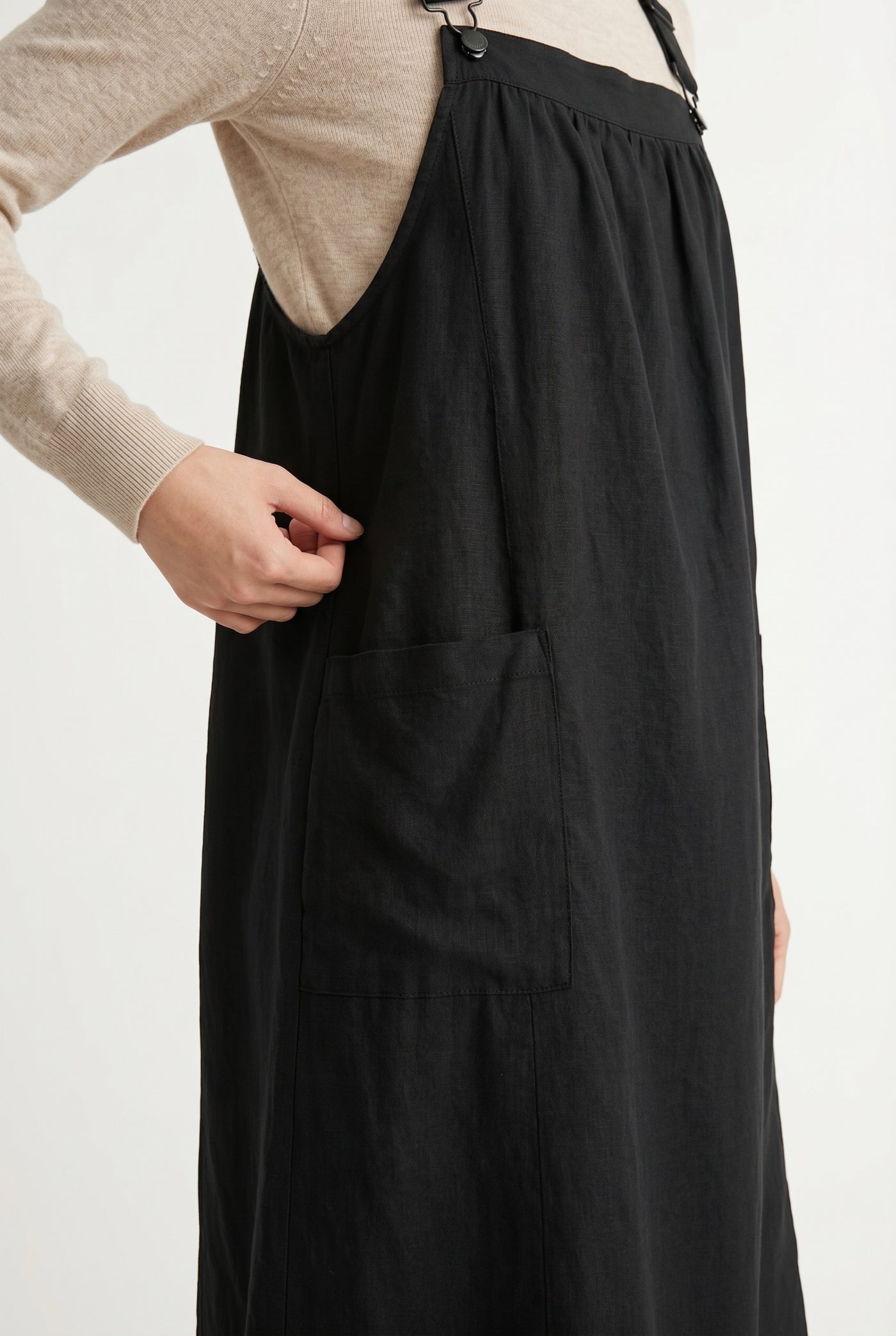 Woman wearing an onyx black midi-length pinafore dress layered over a white long-sleeve top