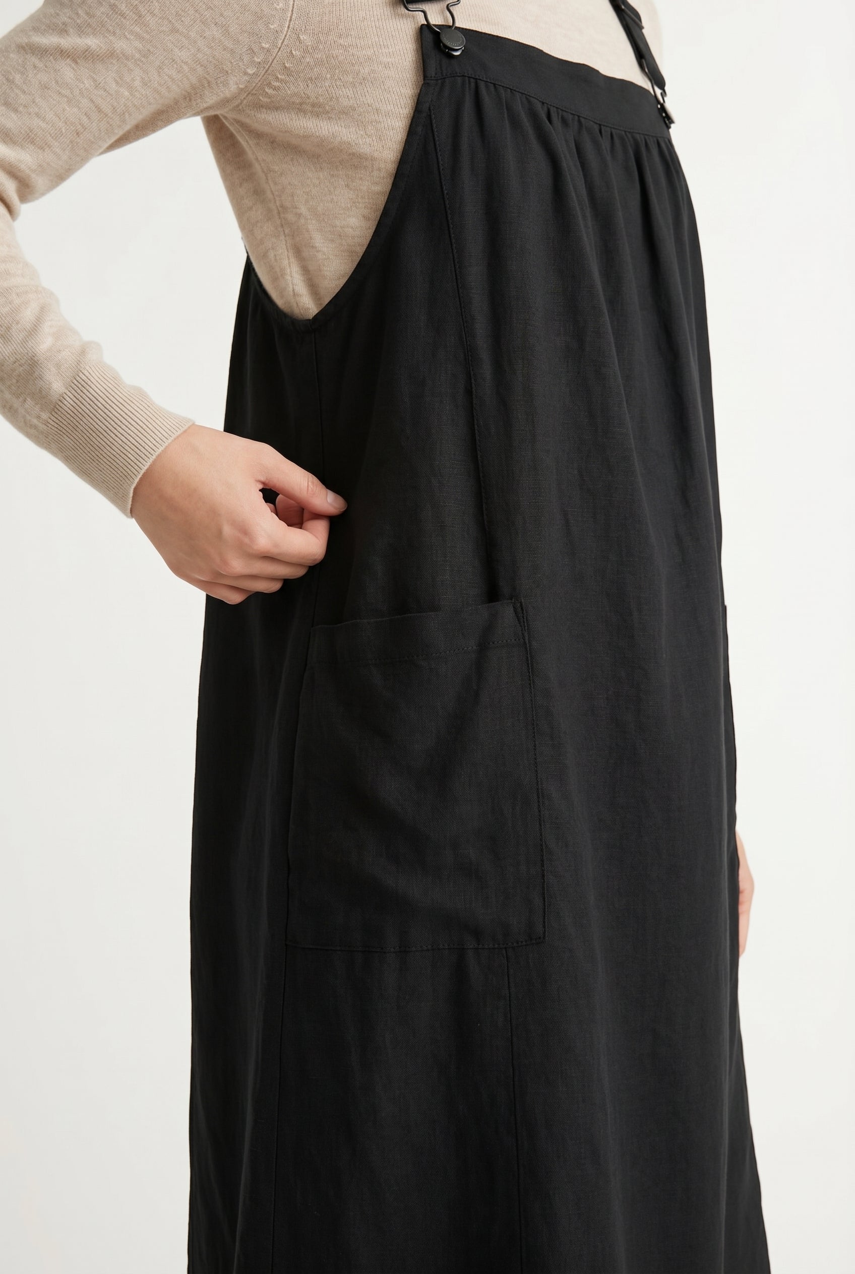 Woman wearing an onyx black midi-length pinafore dress layered over a white long-sleeve top