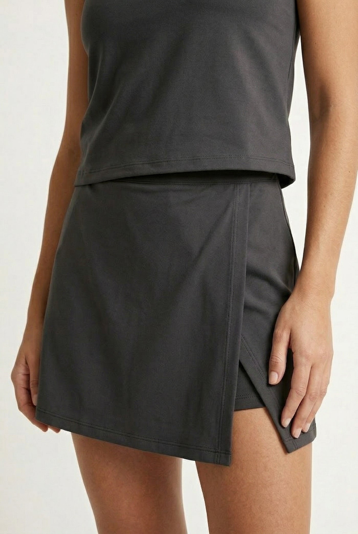 A woman wearing a sleek Black Eyeliner colored sleeveless athletic dress with a mock neck zipper.