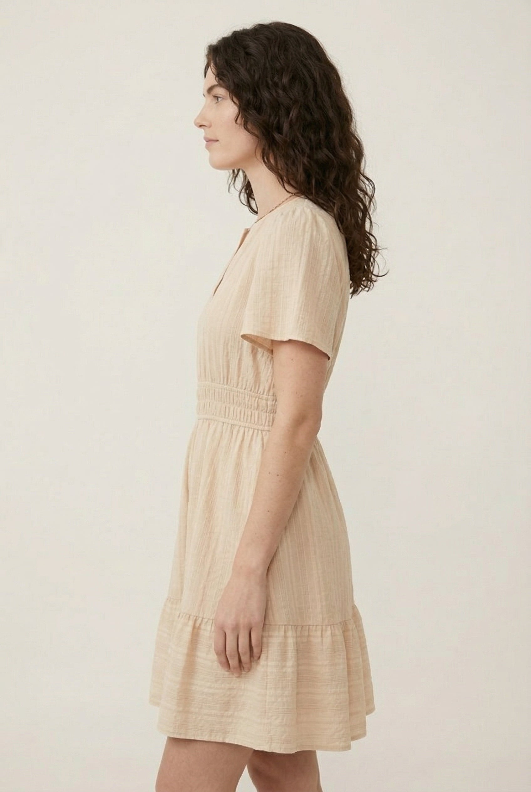 Woman wearing a short sleeve v-neck tiered dress in oat beige color