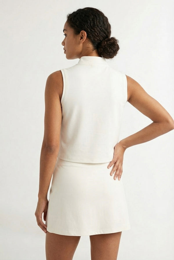 A woman wearing a Birch white sleeveless athletic dress with a high collar and front zipper.