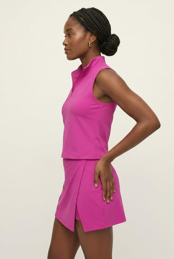 A woman wearing a vibrant Aura Pink sleeveless athletic dress with a zippered high-neck design.