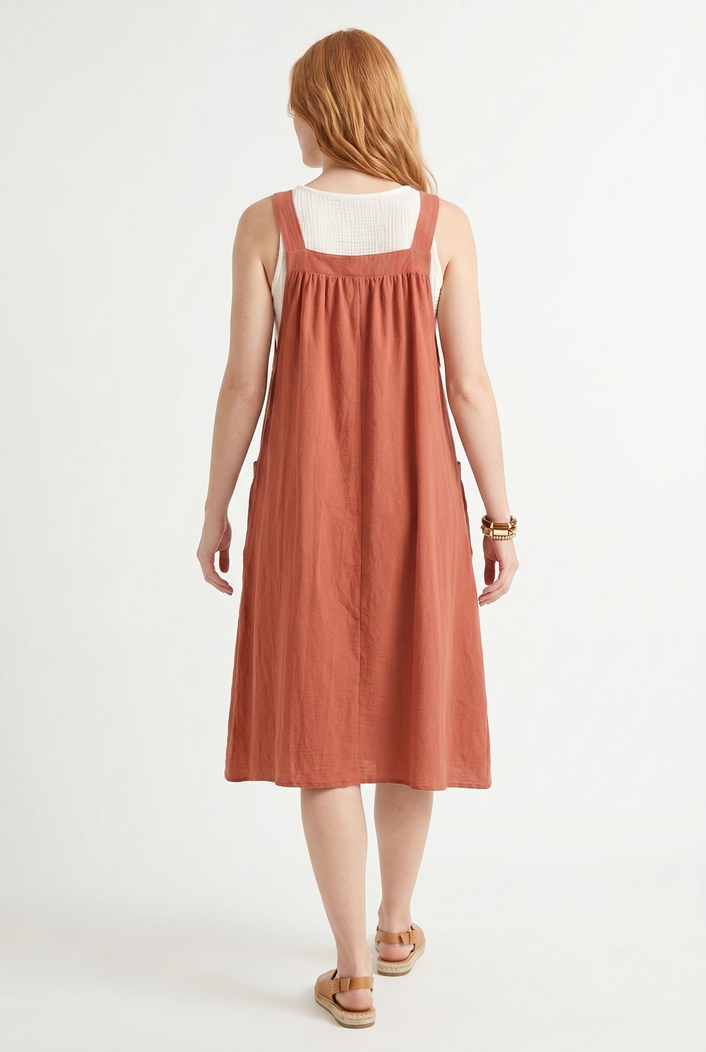 Woman wearing a burnt sienna orange midi-length pinafore dress layered over a white long-sleeve top