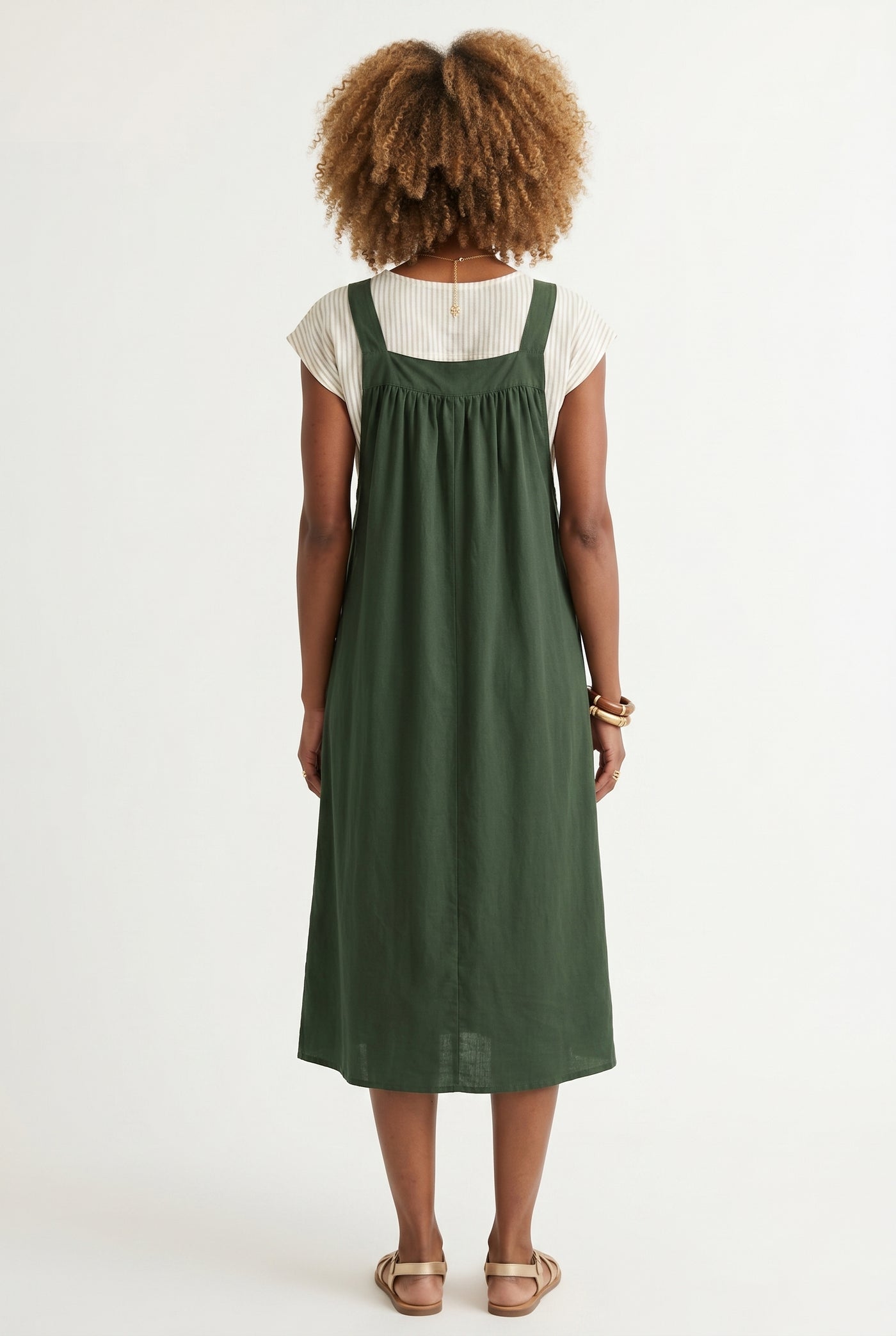Woman wearing a scarab dark green midi-length pinafore dress layered over a white long-sleeve top