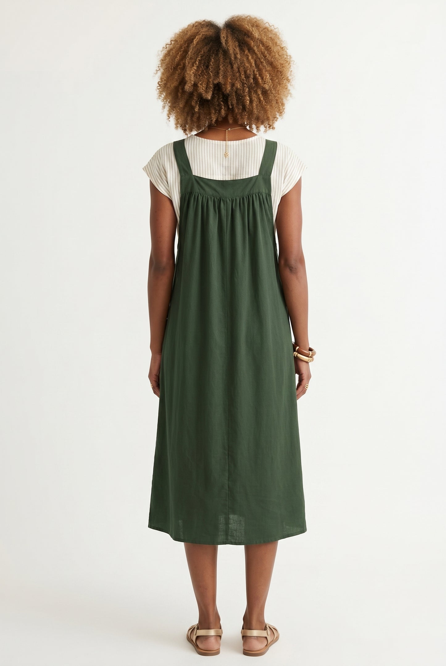Woman wearing a scarab dark green midi-length pinafore dress layered over a white long-sleeve top