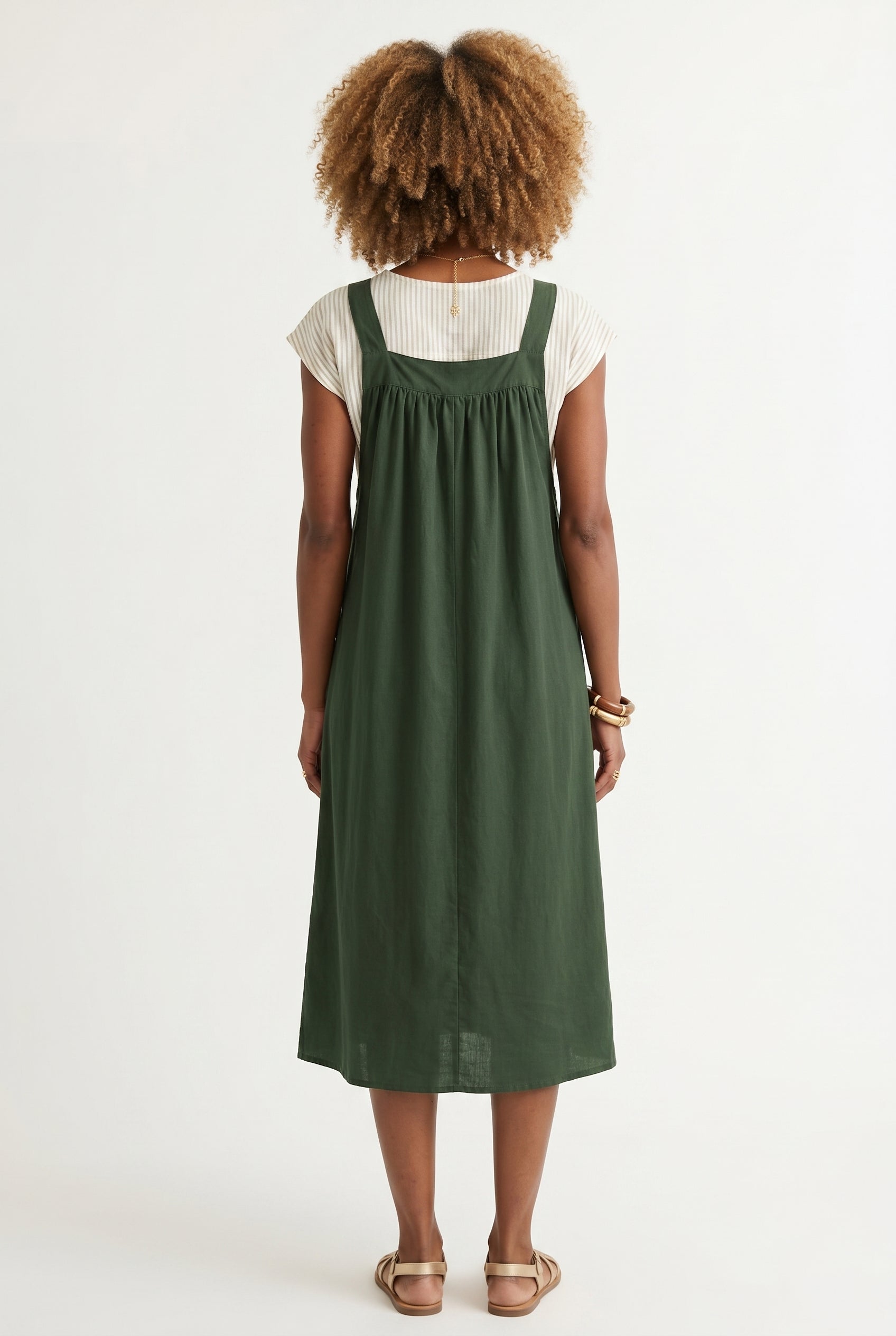 Woman wearing a scarab dark green midi-length pinafore dress layered over a white long-sleeve top