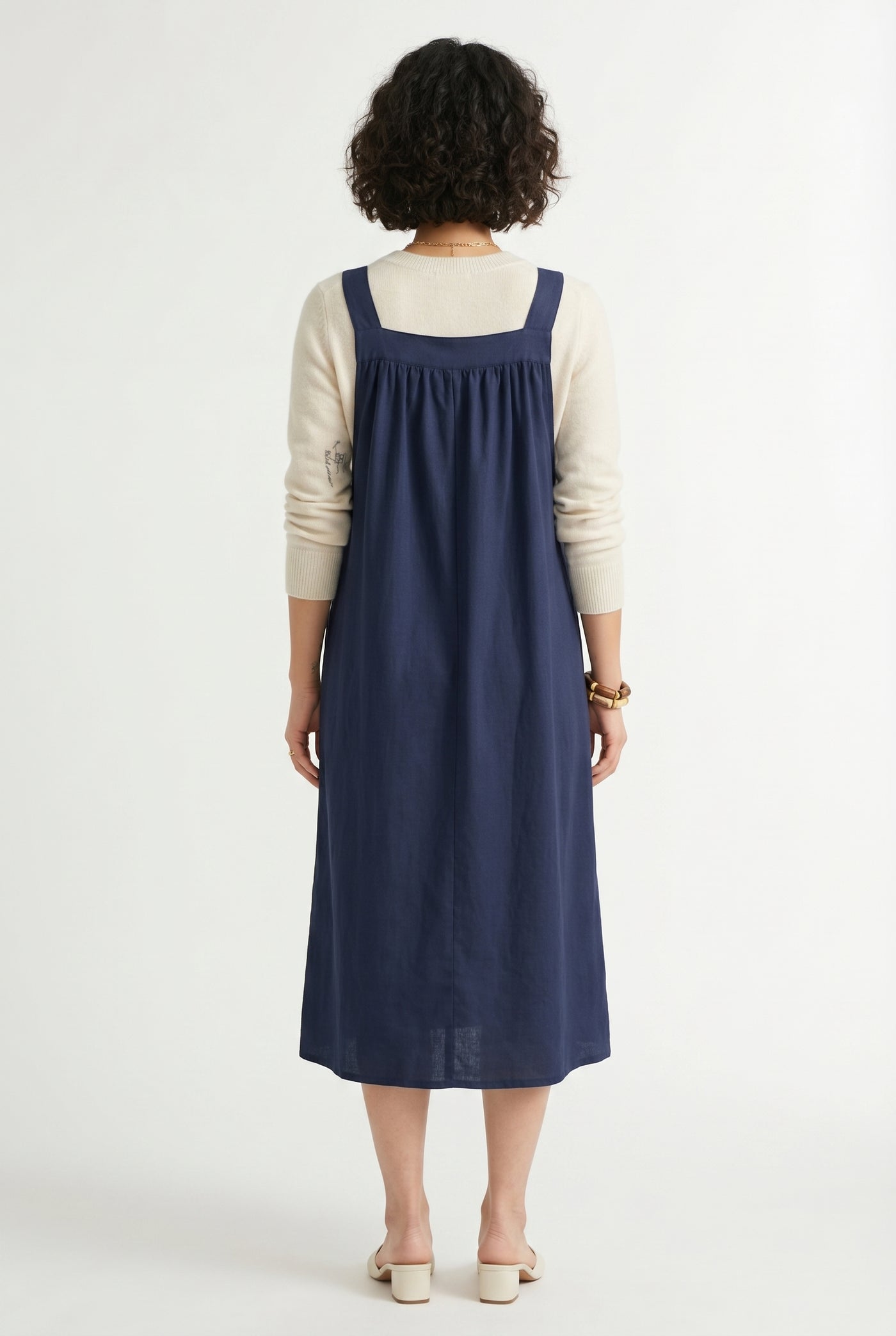 Woman wearing a total eclipse dark navy blue midi-length pinafore dress layered over a white long-sleeve top