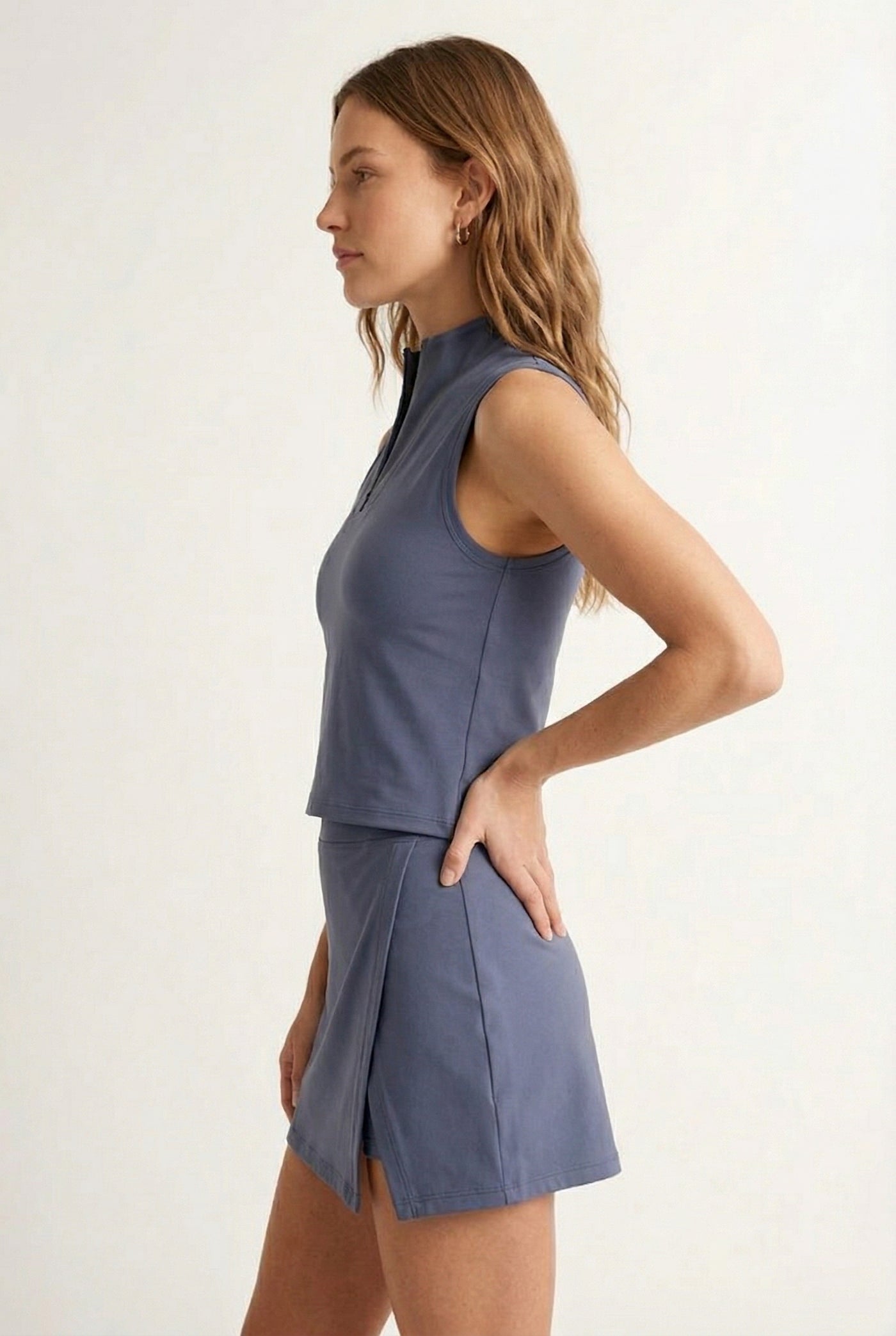 A woman modeling a Chambray blue sleeveless athletic dress with a matching skirt and zip-up collar.
