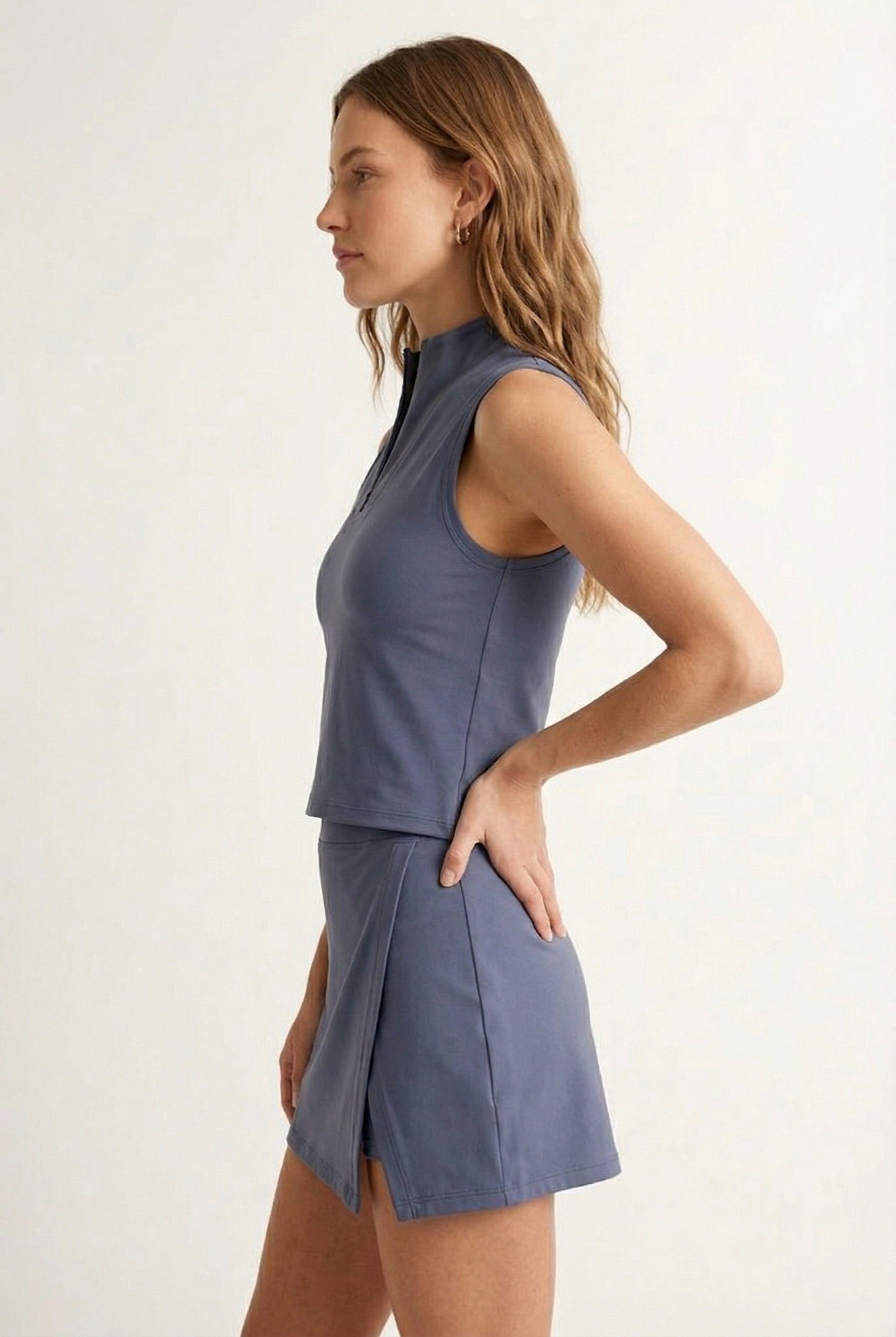 A woman modeling a Chambray blue sleeveless athletic dress with a matching skirt and zip-up collar.