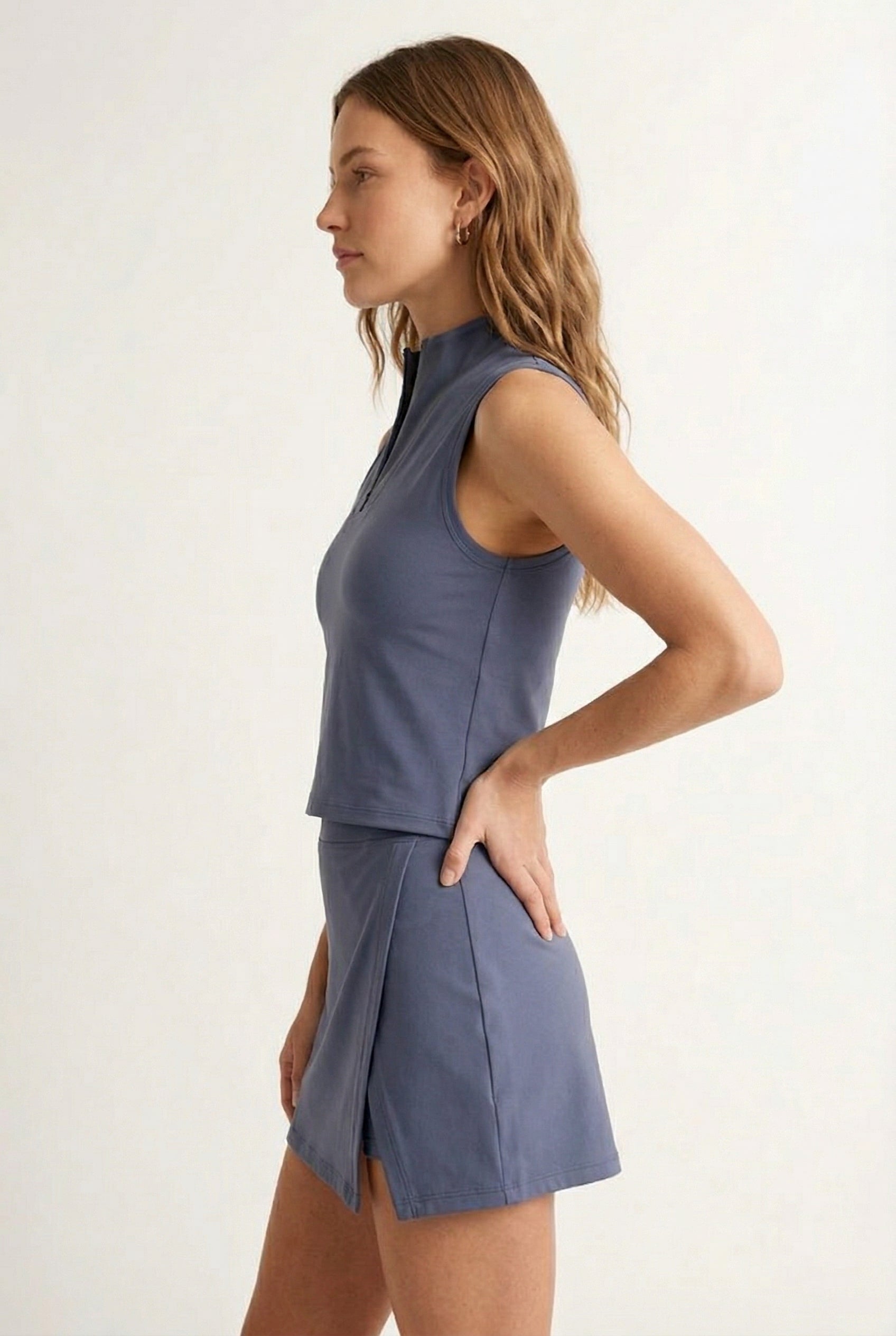 A woman modeling a Chambray blue sleeveless athletic dress with a matching skirt and zip-up collar.
