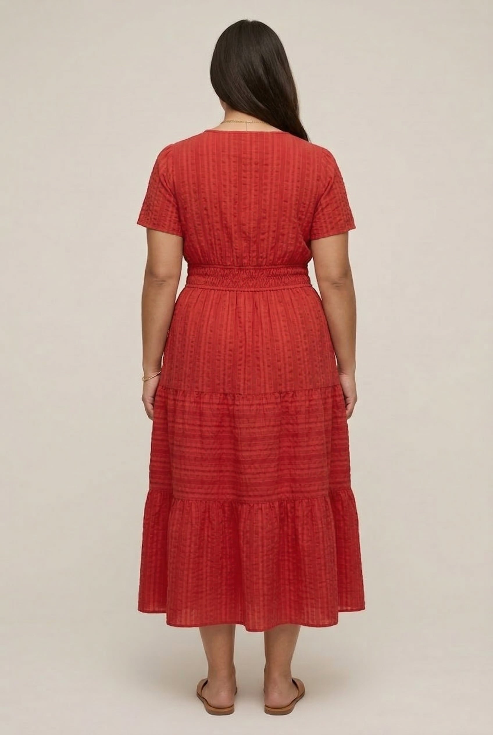 A woman modeling a Cinnabar red short-sleeve midi dress with a button-down front and tiered skirt.