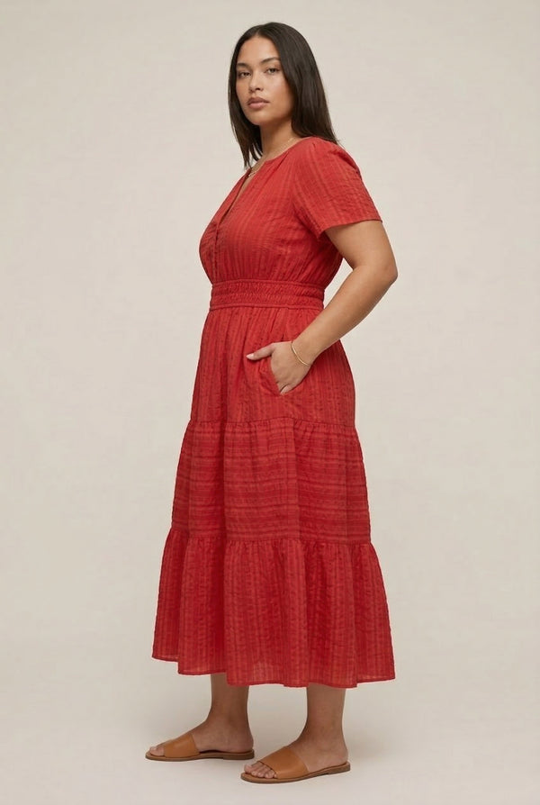 A woman modeling a Cinnabar red short-sleeve midi dress with a button-down front and tiered skirt.