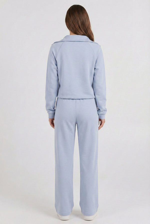 Woman wearing the LOHNR Élan Set in Cloud Blue, featuring a smooth, sweatshirt-material half-zip pullover and matching structured pants.