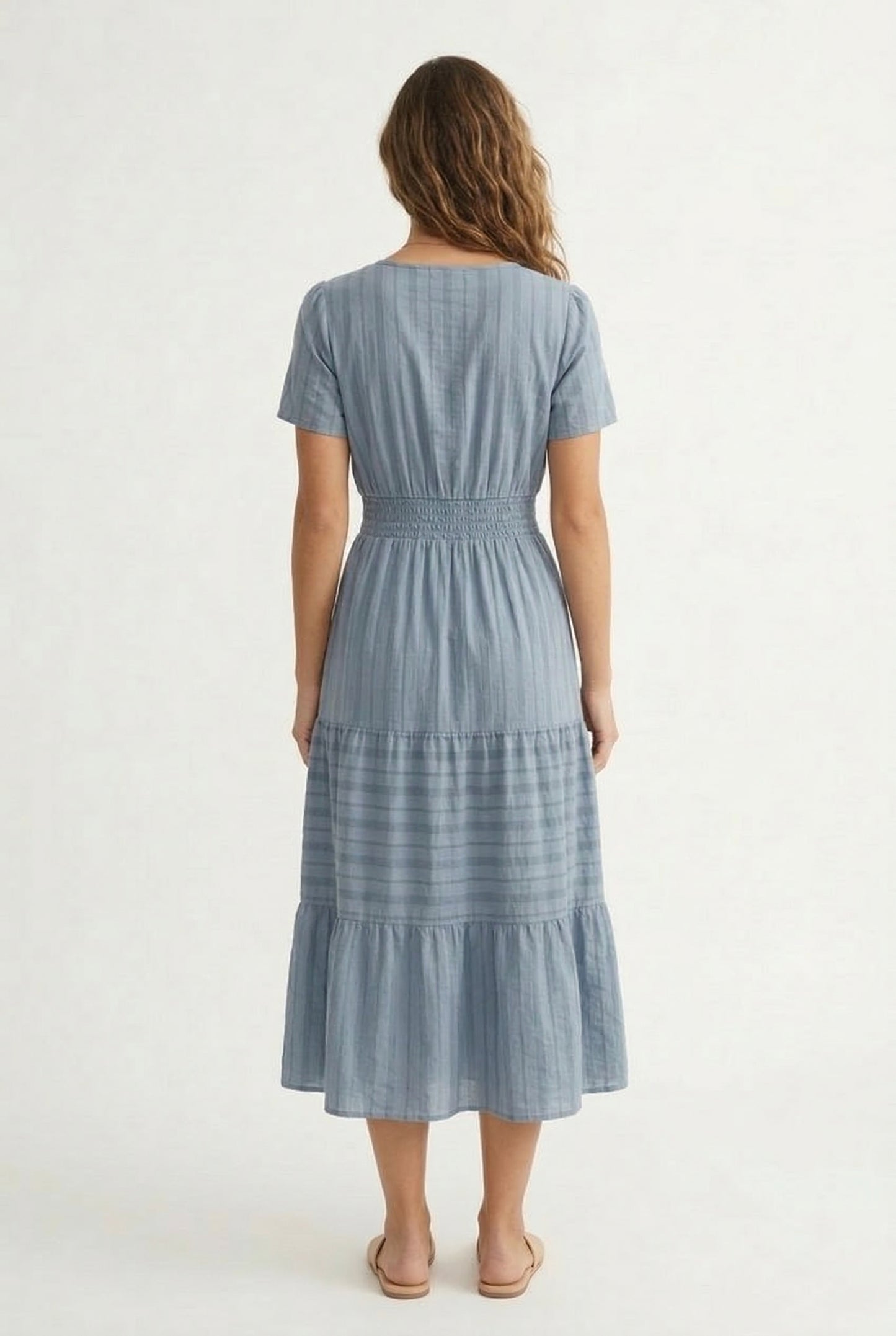 A woman wearing a Cloud Blue short-sleeve midi dress with a button-down front and tiered skirt.