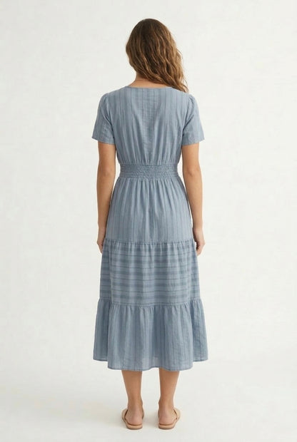 A woman wearing a Cloud Blue short-sleeve midi dress with a button-down front and tiered skirt.