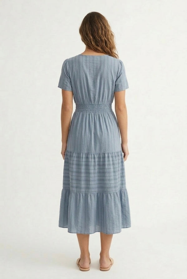 A woman wearing a Cloud Blue short-sleeve midi dress with a button-down front and tiered skirt.
