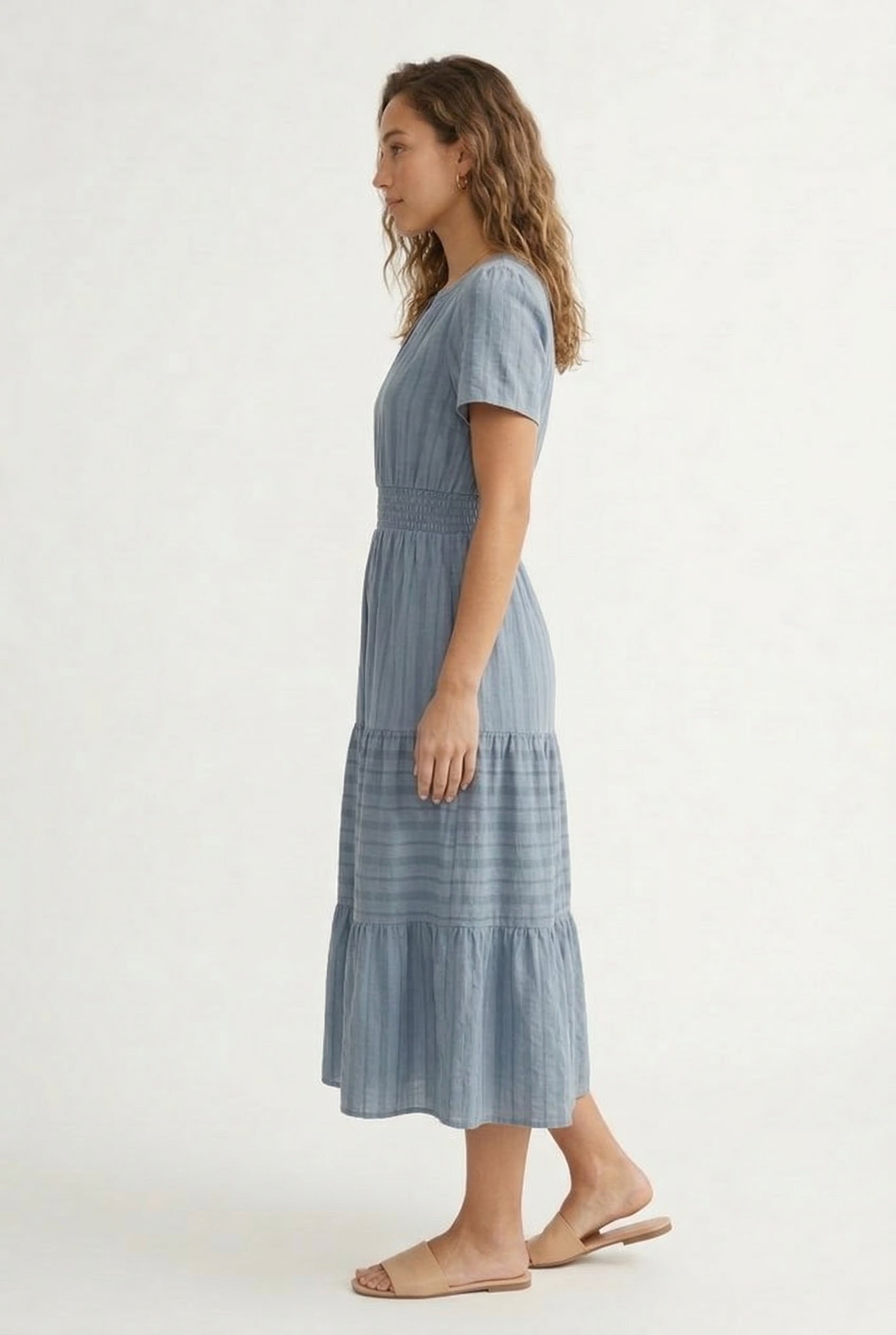 A woman wearing a Cloud Blue short-sleeve midi dress with a button-down front and tiered skirt.