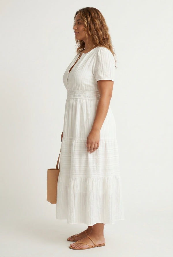 A woman wearing a Cloud White short-sleeve midi dress with a button-down front and tiered skirt.