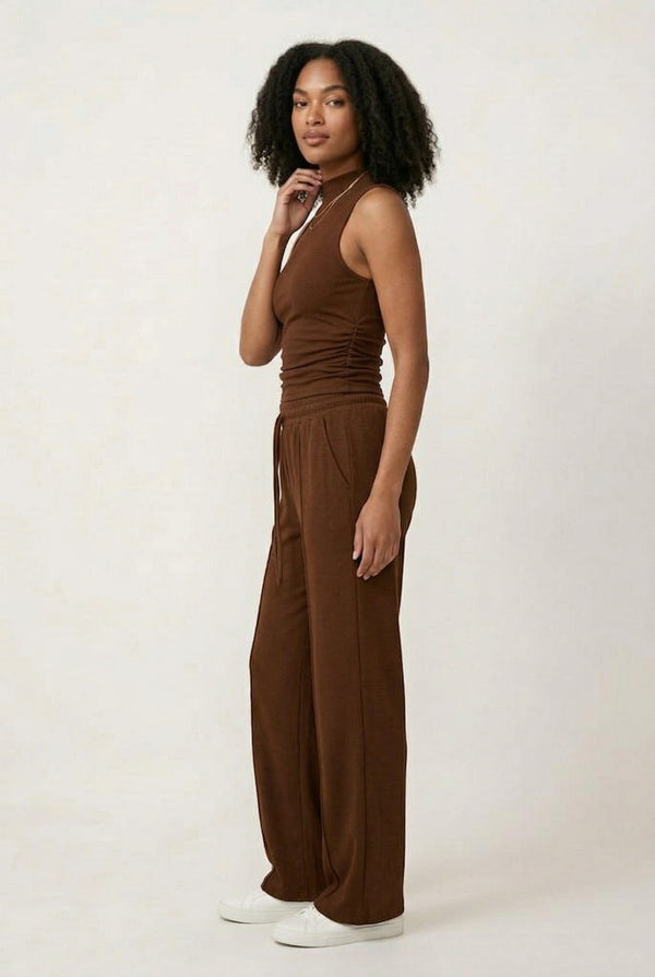 Woman wearing a warm cognac brown sleeveless jumpsuit with wide legs.