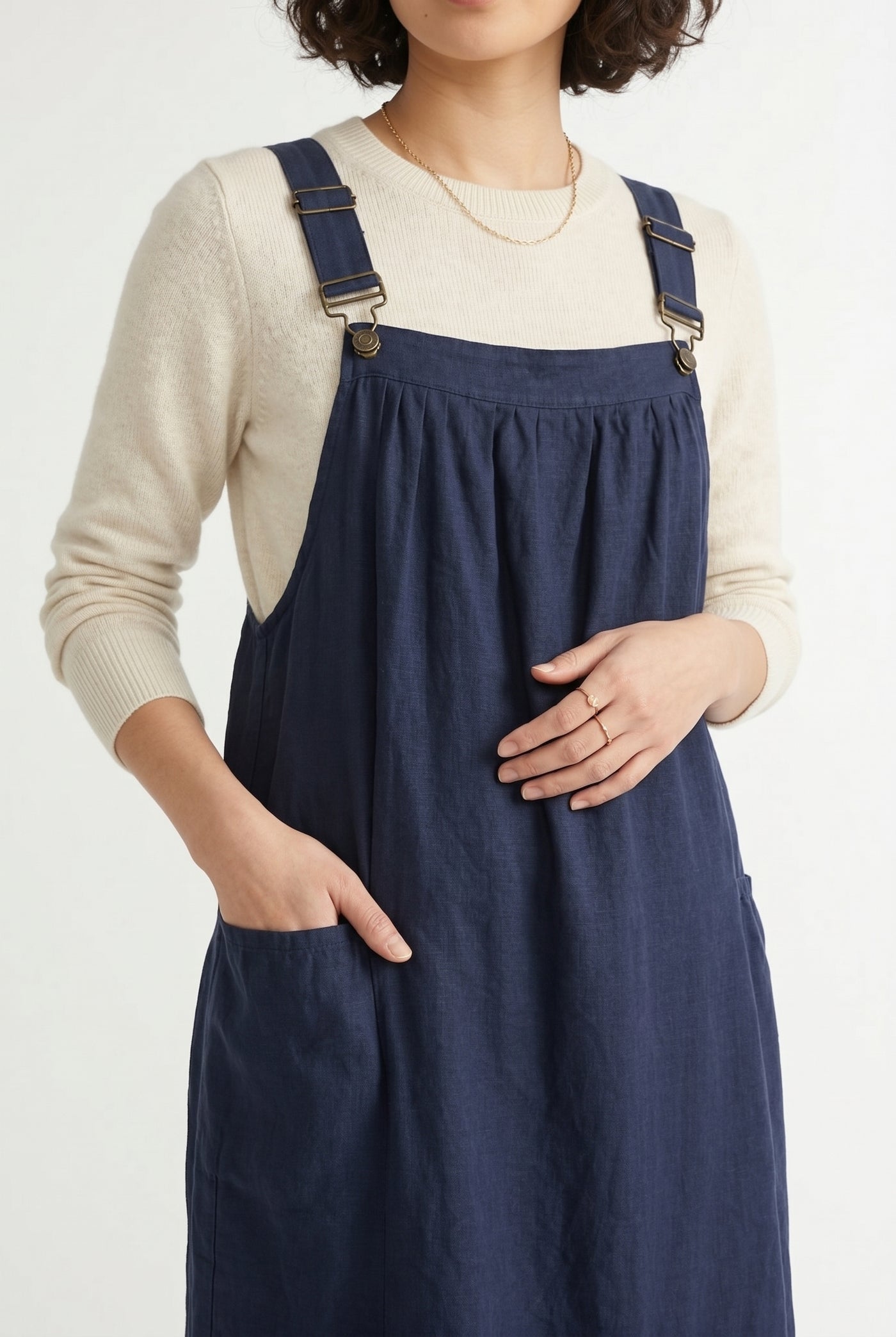 Woman wearing a total eclipse dark navy blue midi-length pinafore dress layered over a white long-sleeve top