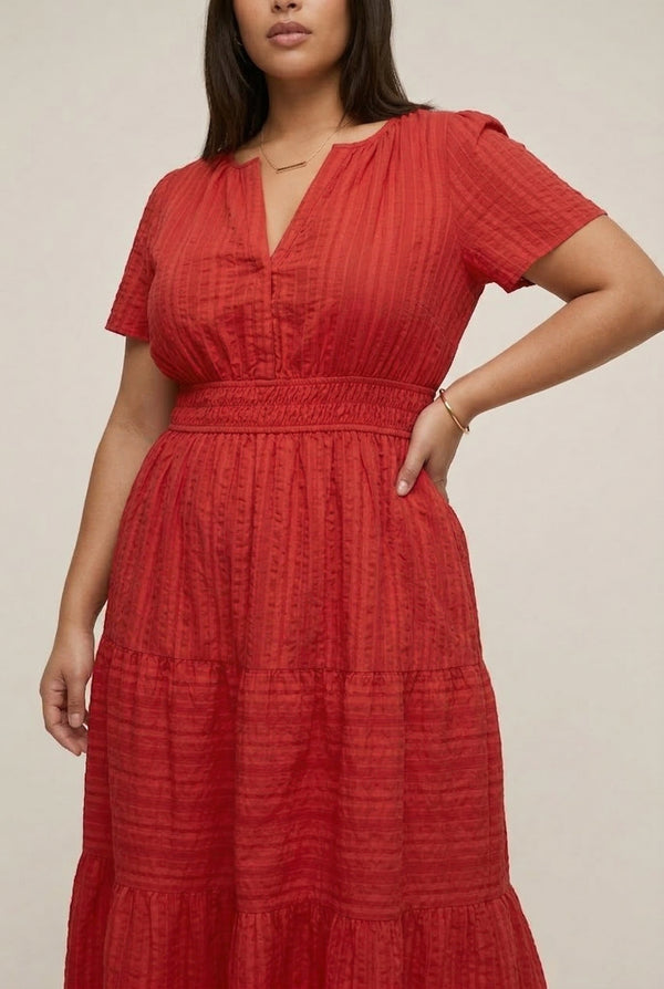 A woman modeling a Cinnabar red short-sleeve midi dress with a button-down front and tiered skirt.