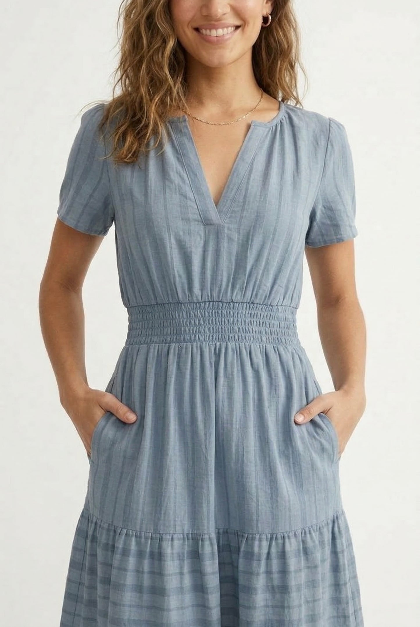A woman wearing a Cloud Blue short-sleeve midi dress with a button-down front and tiered skirt.