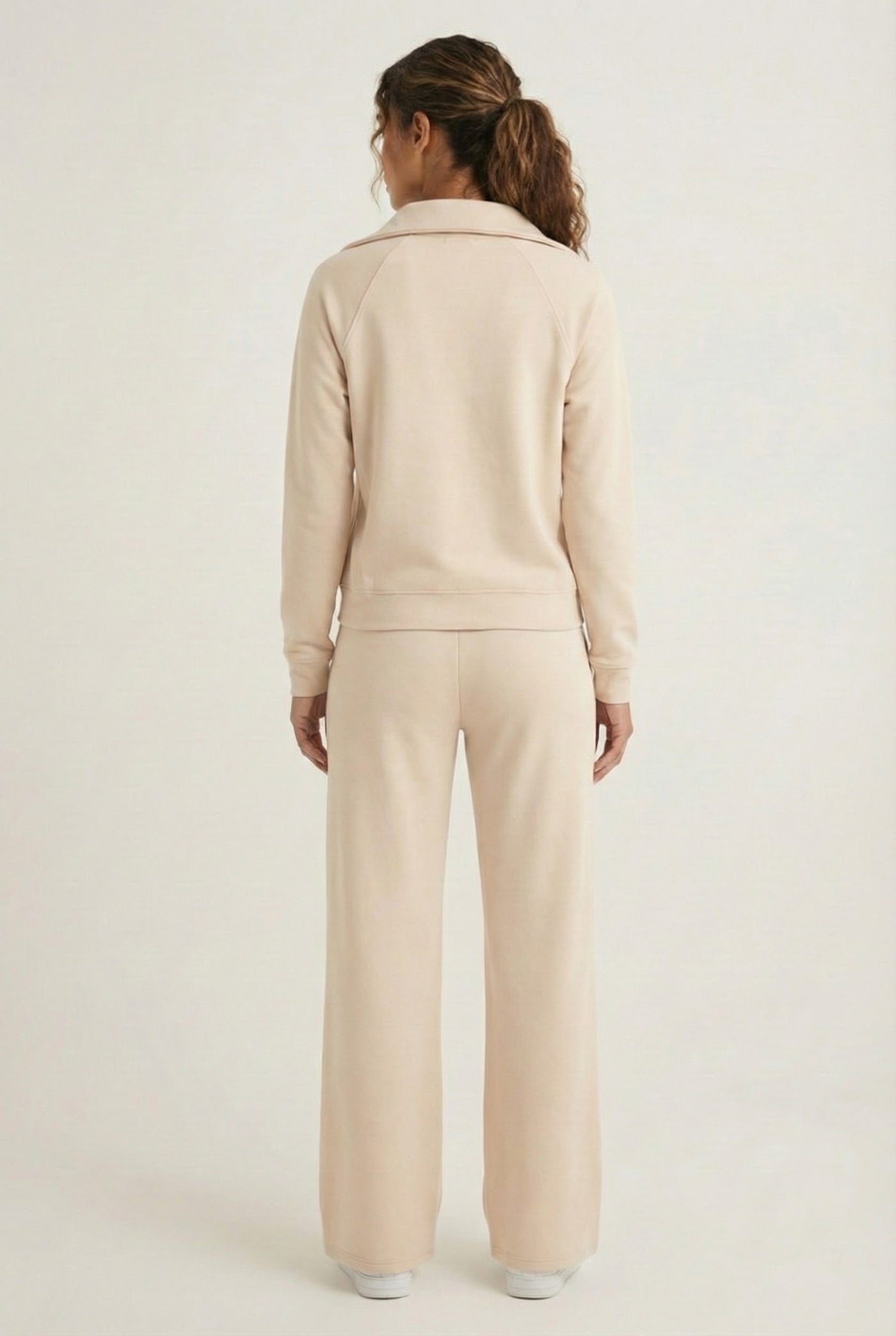 Woman wearing the LOHNR Élan Set in Soft Sand, featuring a smooth, sweatshirt-material half-zip pullover and matching structured pants.