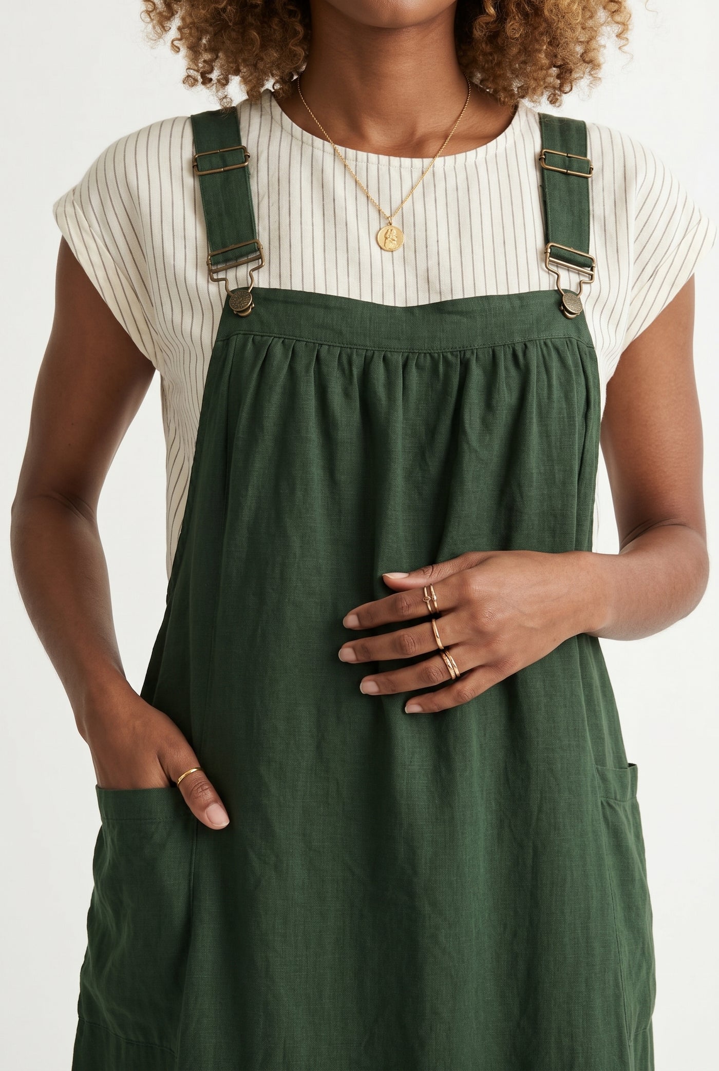 Woman wearing a scarab dark green midi-length pinafore dress layered over a white long-sleeve top