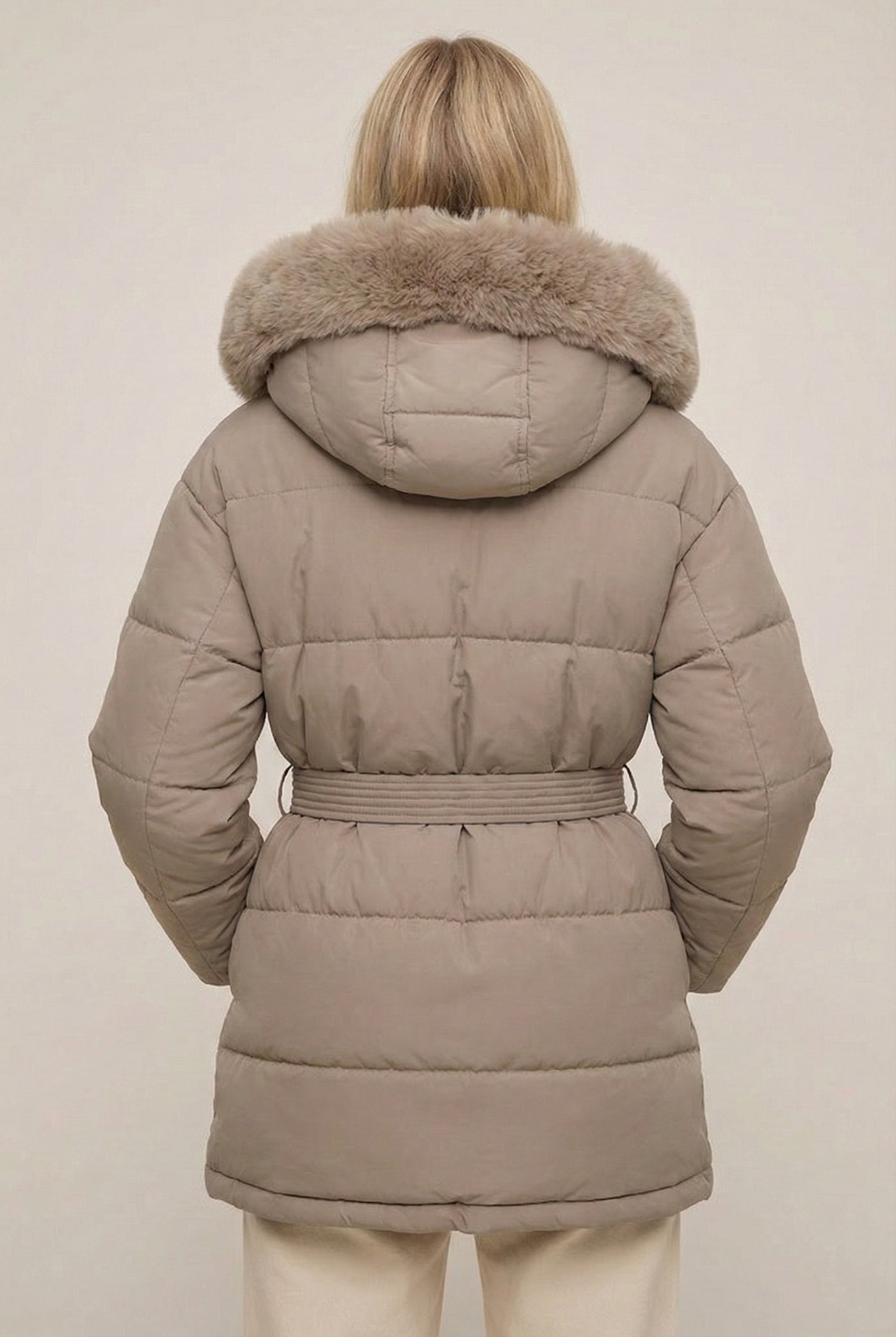 Woman modeling the belted Aspen puffer jacket in Fawn by LOHNR, featuring a detachable faux fur hood.