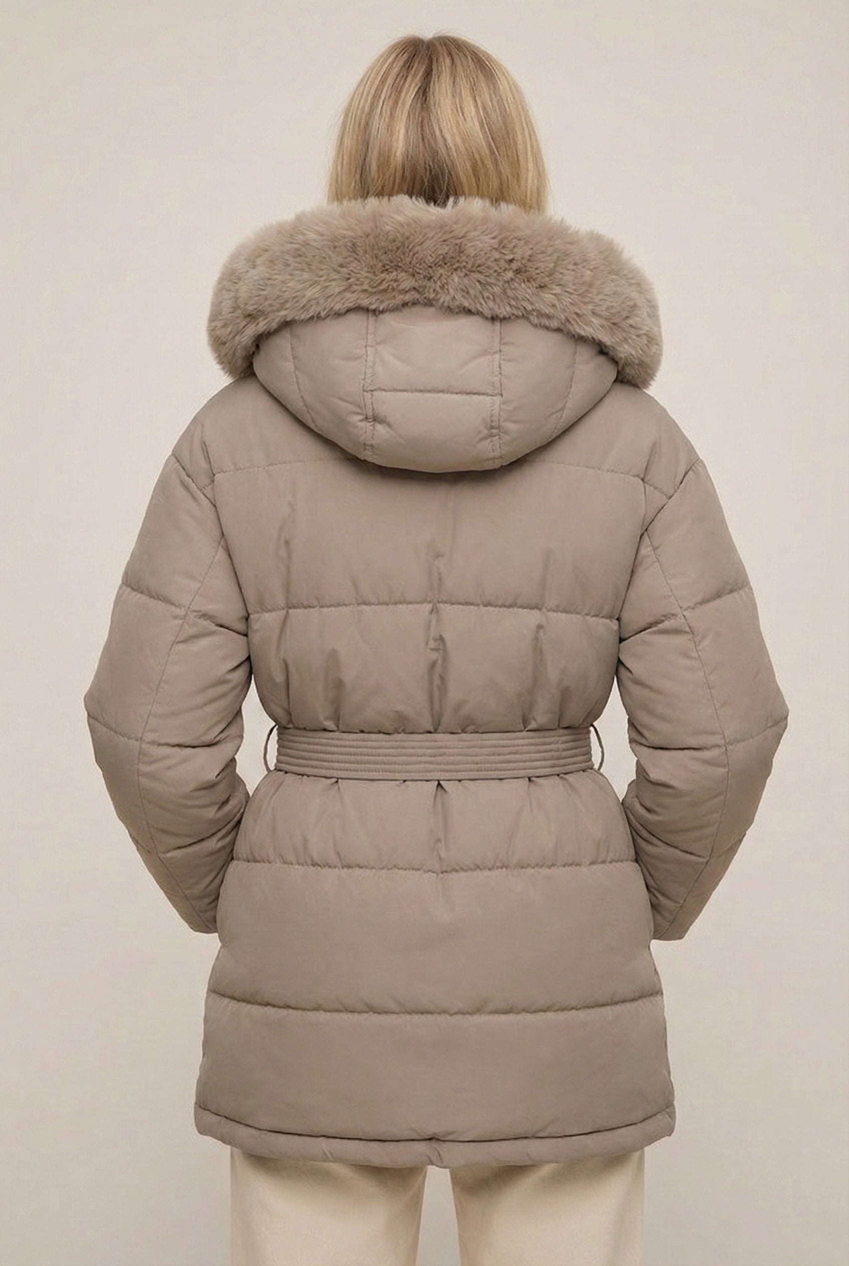 Woman modeling the belted Aspen puffer jacket in Fawn by LOHNR, featuring a detachable faux fur hood.