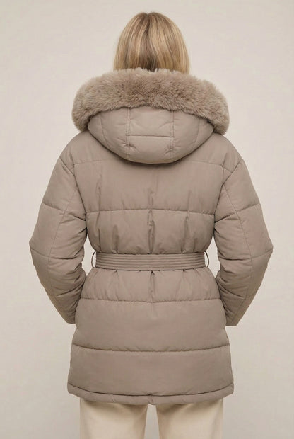 Woman modeling the belted Aspen puffer jacket in Fawn by LOHNR, featuring a detachable faux fur hood.