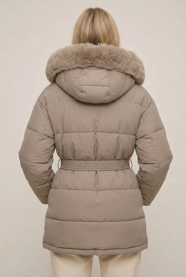 Woman modeling the belted Aspen puffer jacket in Fawn by LOHNR, featuring a detachable faux fur hood.