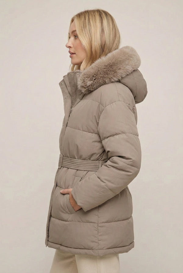 Woman modeling the belted Aspen puffer jacket in Fawn by LOHNR, featuring a detachable faux fur hood.
