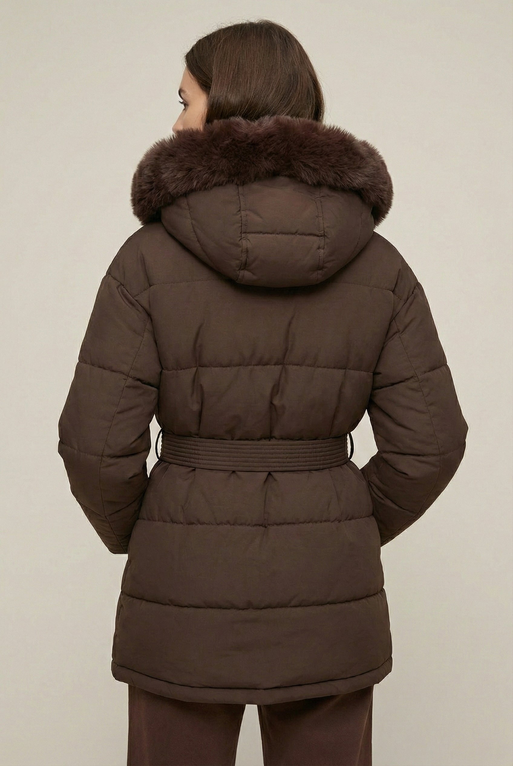 Woman modeling the belted Aspen puffer jacket in Mocha by LOHNR, featuring a detachable faux fur hood.