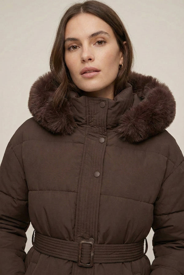 Woman modeling the belted Aspen puffer jacket in Mocha by LOHNR, featuring a detachable faux fur hood.