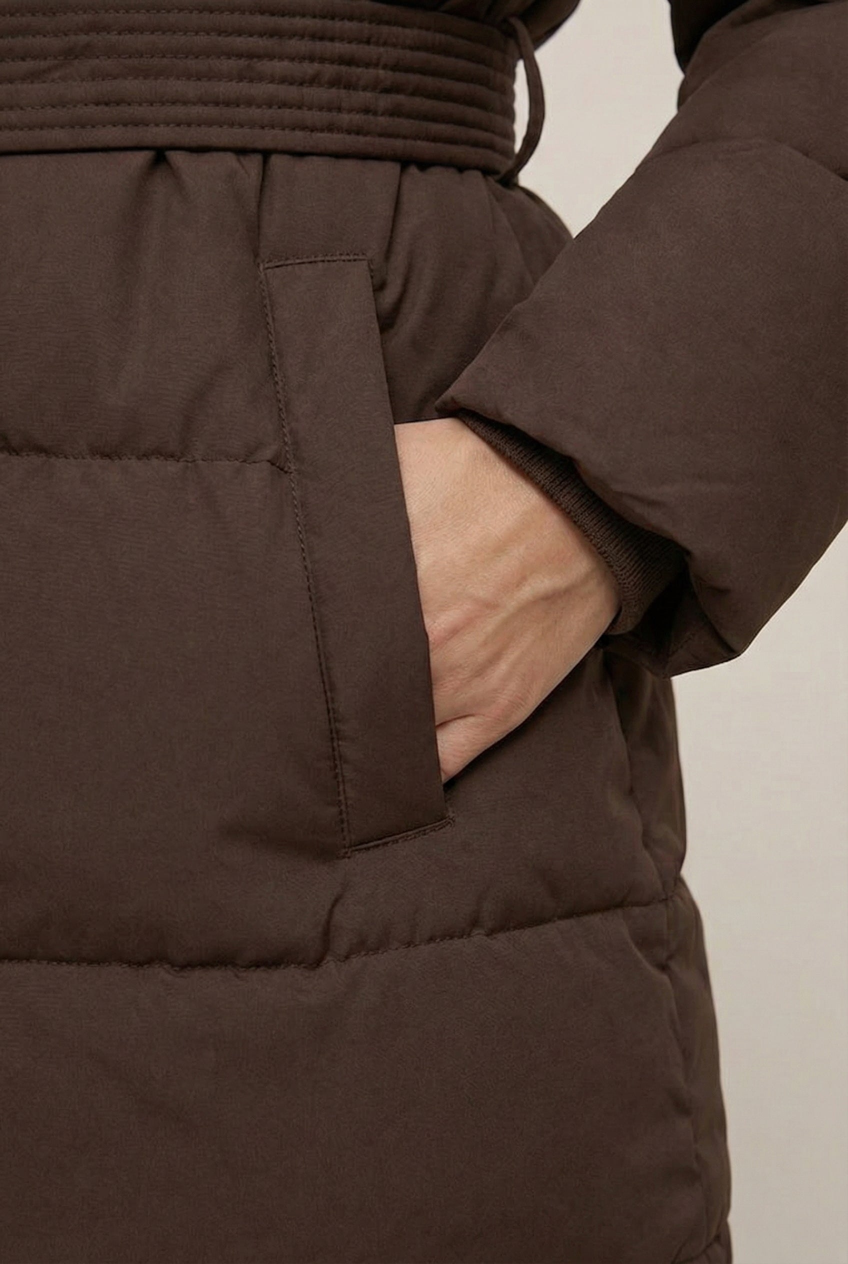 Woman modeling the belted Aspen puffer jacket in Mocha by LOHNR, featuring a detachable faux fur hood.