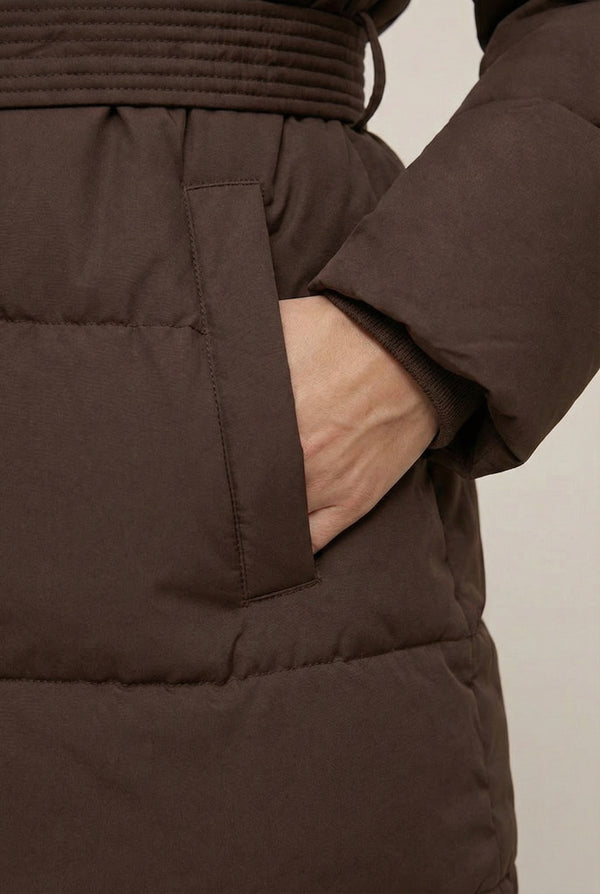 Woman modeling the belted Aspen puffer jacket in Mocha by LOHNR, featuring a detachable faux fur hood.