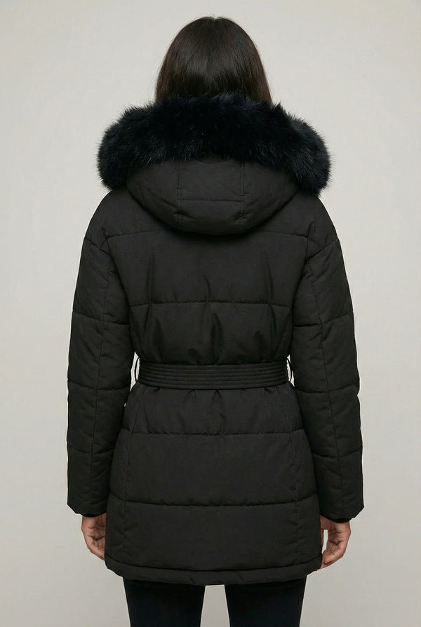 Woman modeling the belted Aspen puffer jacket in Onyx by LOHNR, featuring a detachable faux fur hood.