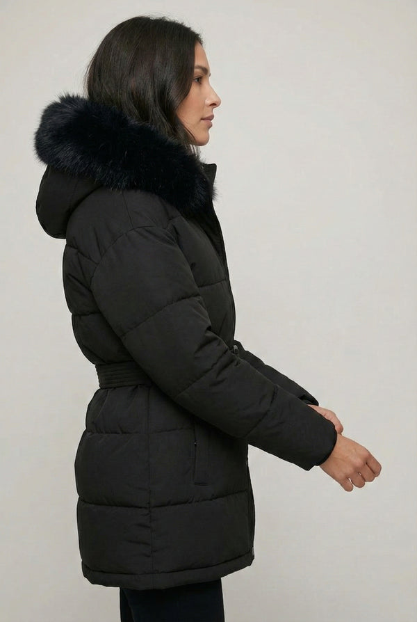 Woman modeling the belted Aspen puffer jacket in Onyx by LOHNR, featuring a detachable faux fur hood.