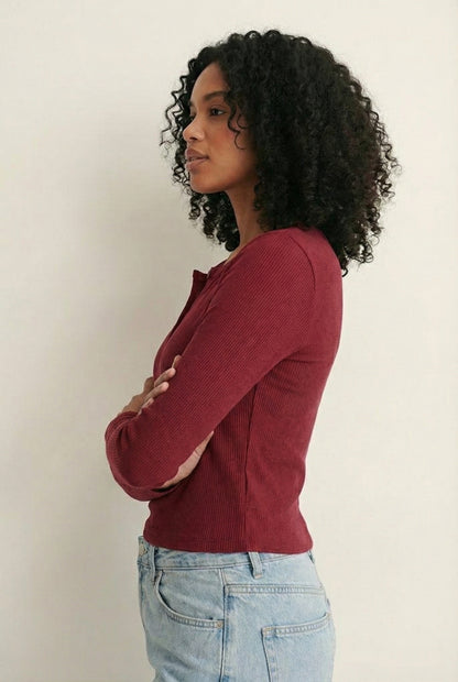 Woman wearing the LOHNR Haven Henley in Cabernet, a deep burgundy ribbed long-sleeve top with a button placket, styled for effortless everyday luxury.