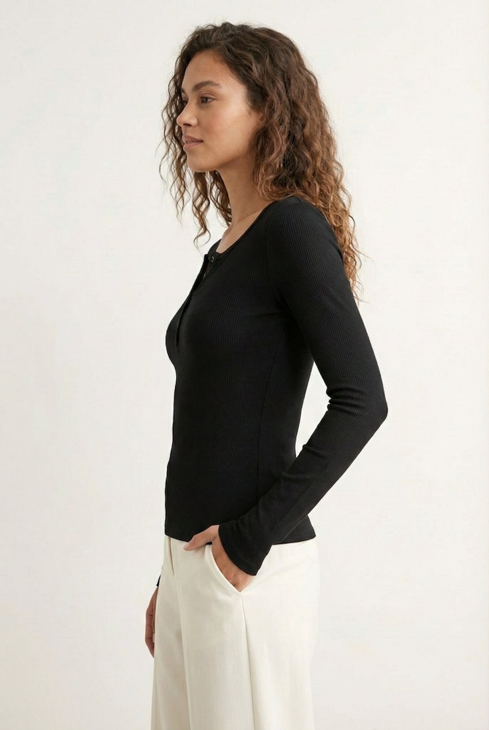 Woman wearing the LOHNR Haven Henley in Rich Black, a sleek black ribbed long-sleeve top with a button placket, styled for effortless everyday luxury.
