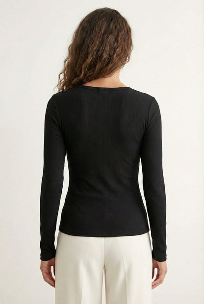 Woman wearing the LOHNR Haven Henley in Rich Black, a sleek black ribbed long-sleeve top with a button placket, styled for effortless everyday luxury.