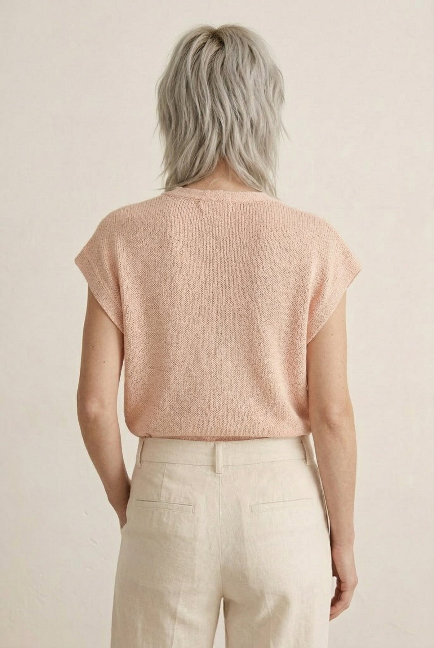 Woman modeling the LOHNR short sleeve v-neck knit top in washed apricot featuring a button-down front.