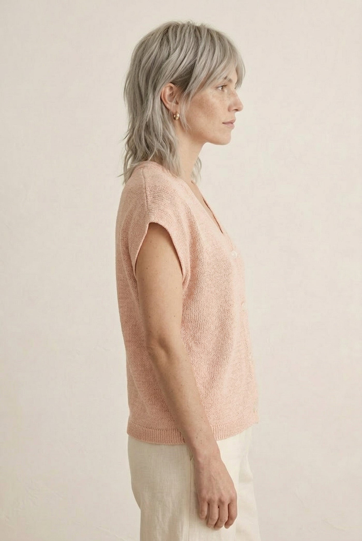 Woman modeling the LOHNR short sleeve v-neck knit top in washed apricot featuring a button-down front.