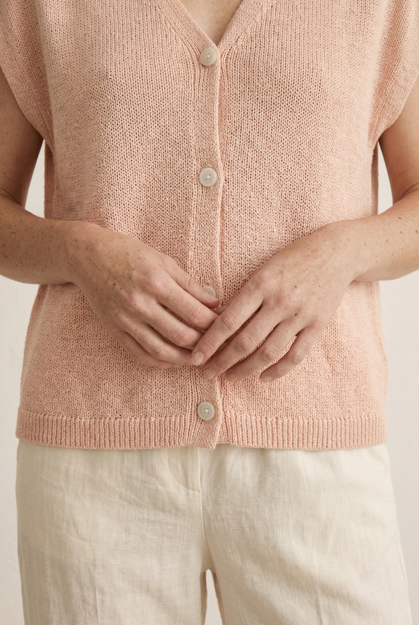 Woman modeling the LOHNR short sleeve v-neck knit top in washed apricot featuring a button-down front.