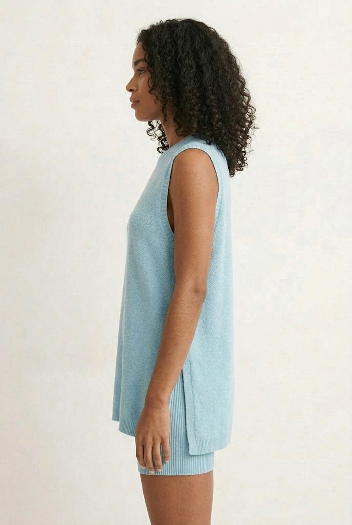 A woman wearing the LOHNR Slouch Tunic Set in Iced Sky, a soft pale blue sleeveless tunic and shorts set.
